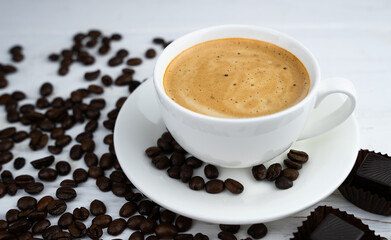 A cup of aromatic coffee and scattered coffee beans on the table. Close-up. Selective focus.