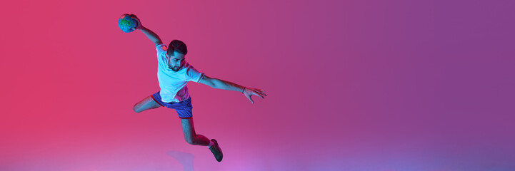 Aerial view. Young man, professional handball player playing isolated over gradient pink background...