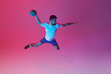Fototapeta na wymiar Top view. In a jump. Young man, professional handball player training, playing isolated over gradient pink background in neon light. Concept of sport, action, motion, championship, sportive lifestyle