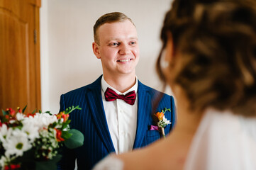 The bride's hand puts on a boutonniere flower on the groom's jacket. Bride puts a buttonhole on a grooms suit. Close up. - obrazy, fototapety, plakaty