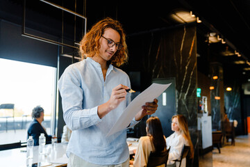 Obraz premium Young businessman writing down notes during meeting in conference room with his colleagues on a background