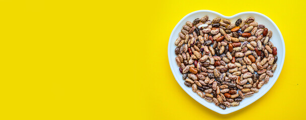 Banner. Dry beans on a white plate in the shape of a heart. Beans in a bowl isolated on a yellow background	
