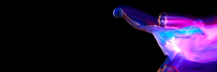Motivation. Young man, professional handball player in motion, playing over black background with...