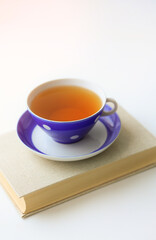 An old vintage book and a polka dot cup on the window. Selective focus.