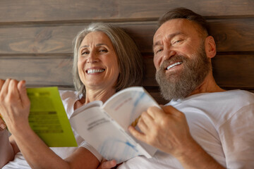 Mature couple spending time in bed and reading a book
