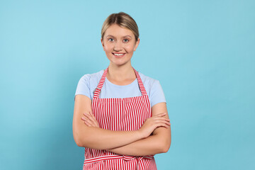 Beautiful young woman in clean striped apron on light blue background