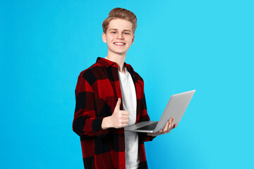 Teenage boy with laptop showing thumb up on light blue background © New Africa