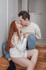 Couple in love kissing on wooden stairs. A red-haired young woman with bare legs in the arms of a man. Feeling, sensuality.