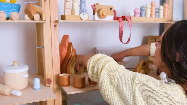 a craftsman girl puts ready-made wooden toys on a shelf in the workshop