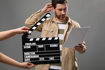 Actor performing while second assistant camera holding clapperboard on grey background, closeup