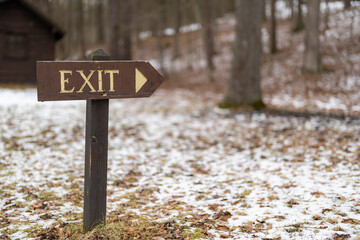 Winter scene with a rustic wooden exit sign with arrow pointing right within a park
