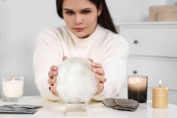 Soothsayer predicting future at table in room, focus on crystal ball
