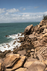rocks on a beach with clear blue water and a military ship on the background