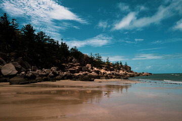 rocks on a beach with clear blue water and a military ship on the background
