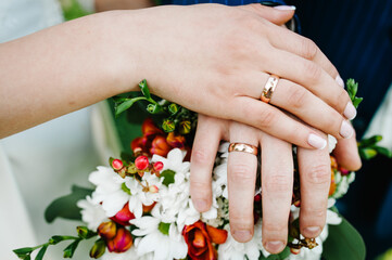 Obraz na płótnie Canvas Newlywed couple holding hands and displaying wedding rings, close up. Hands and rings on the background of bouquet. Top view.