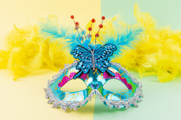 Front view of a venetian carnival turquoise mask with yellow and green background. Colorful blue costume accessory with feathers for party and Venice carnival. Horizontal banner with copy space. 