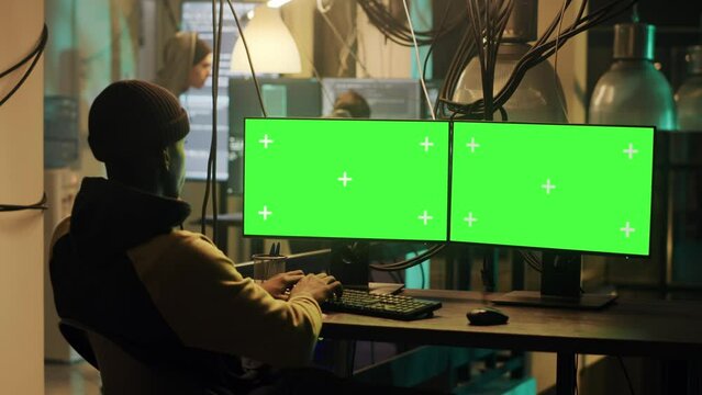 Mysterious criminal using greenscreen display to hack web network, planning phishing attack at night. Man doing illegal activity with isolated chromakey template and mockup, security breach.