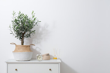 Olive tree in pot and alarm clock on white cabinet in room, space for text. Interior element