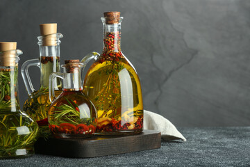 Cooking oil with different spices and herbs in jugs on light grey table. Space for text