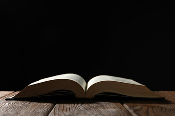 Open Bible on wooden table against black background. Space for text