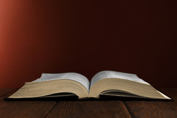 Open Bible on wooden table against brown background. Space for text
