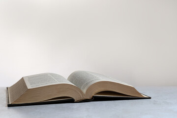 Open hardcover Bible on light grey table, space for text. Religious book