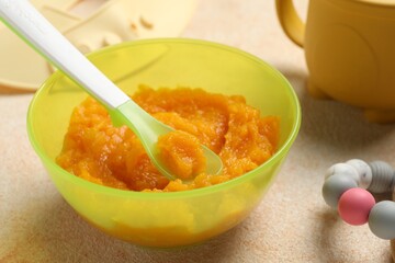 Baby food. Bowl with tasty pumpkin puree on beige textured table, closeup