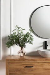 Modern bathroom interior with stylish mirror, eucalyptus branches, vessel sink and wooden vanity