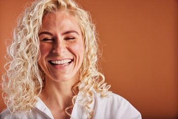 Young blonde woman laughing with her eyes closed on an orange background