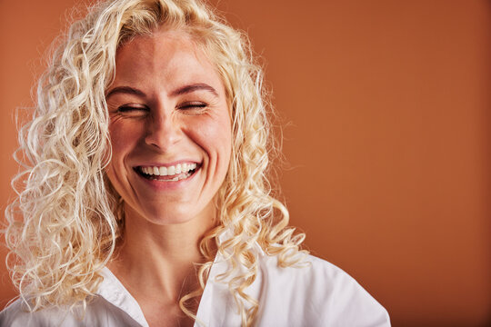 Young blonde woman laughing with her eyes closed on an orange background