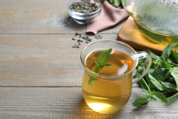 Cup with hot aromatic mint tea on wooden table, space for text