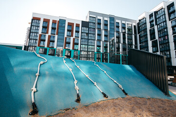 A courtyard of high-rise buildings with a modern and large playground made of wood and plastic on a summer day without people. Empty outdoor playground 