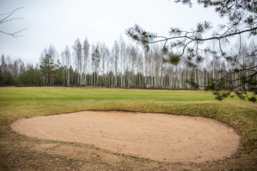Golf course with beautiful sky and sand trap. Scenic panoramic view of golf fairway with bunker. Golf field with pines