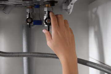 Woman turning on valve of gas boiler, closeup