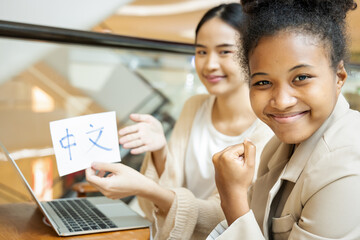 Happy smiling African woman learning Chinese language with her female teacher, holding Chinese...