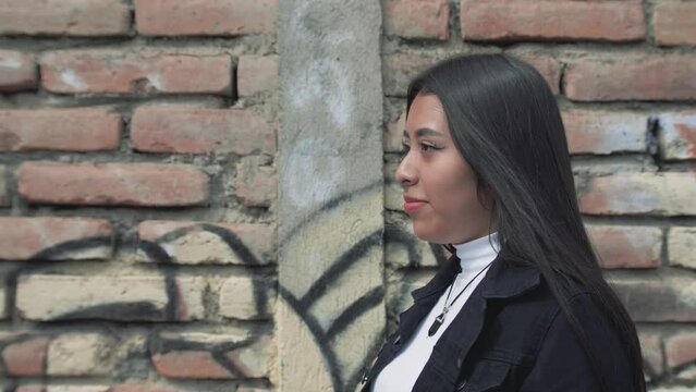 Close up of a hispanic walking along red brick walls with graffiti in the city