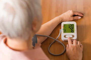An elderly woman measures blood pressure with an electrical device. A pensioner uses a tonometer....