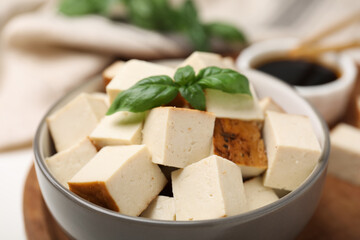 Bowl of smoked tofu cubes, soy sauce and basil on wooden tray, closeup