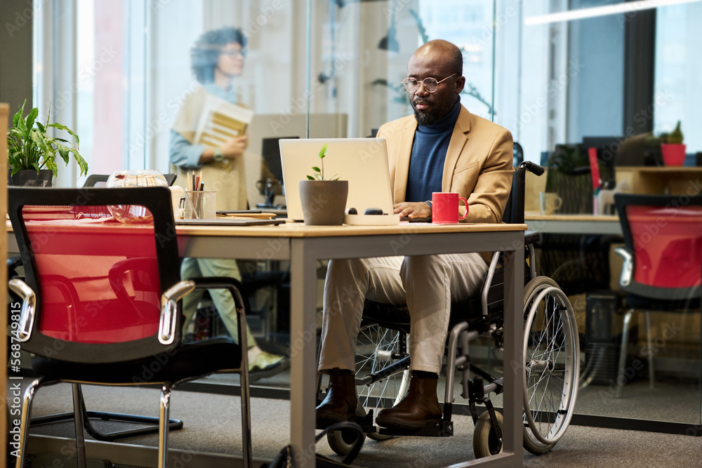Aufkleber young african american businessman with disability sitting in wheelchair by table and networking in 