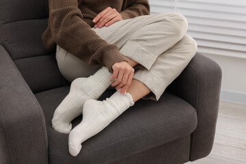 Woman in warm socks relaxing on armchair at home, closeup