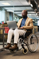 Young serious male analyst wearing casualwear with laptop on his knees sitting in wheelchair and...