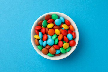 Bowl with tasty colorful candies on blue background, top view