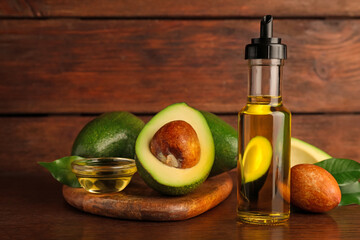 Glass bottle of cooking oil and fresh avocados on wooden table