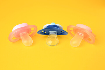 Colorful baby pacifiers on bright orange background