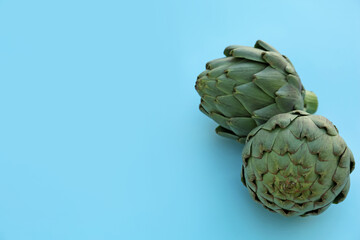 Obraz premium Whole fresh raw artichokes on light blue background. Space for text
