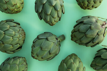 Obraz premium Whole fresh raw artichokes on green background, flat lay