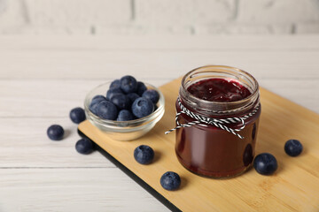 Jar of delicious blueberry jam and fresh berries on white wooden table