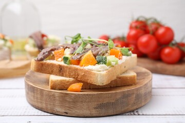 Delicious toasts with anchovies, cream cheese, bell peppers and cucumbers on white wooden table, closeup