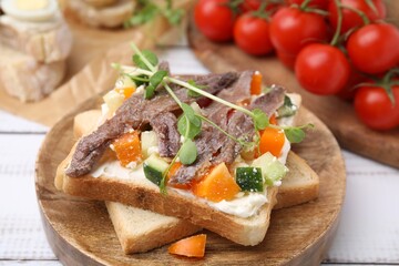 Delicious toasts with anchovies, cream cheese, bell peppers and cucumbers on white wooden table, closeup