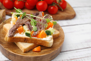 Delicious toasts with anchovies, cream cheese, bell peppers and cucumbers on white wooden table, closeup. Space for text